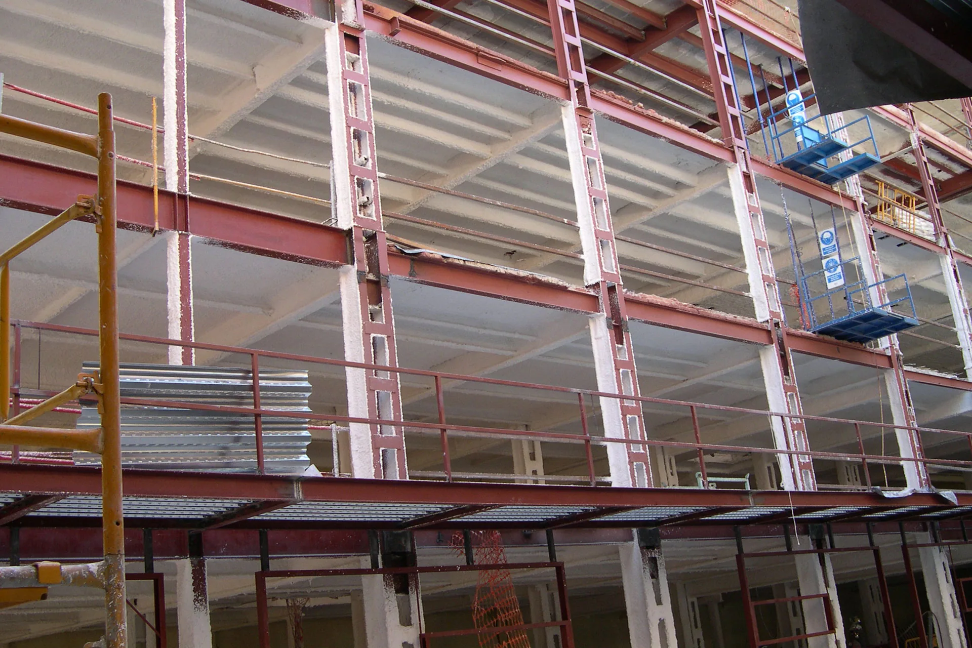 Pilares y vigas metálicas imprimados en rojo con mortero ignífugo proyectado en obra